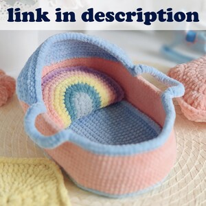 Pu&ograve; includere: Una culla per neonati in crochet rosa e blu con un cuscino in crochet arcobaleno all'interno. La culla &egrave; realizzata in filato morbido e ha un manico su ogni lato.