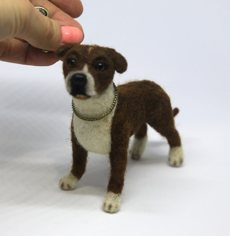 May include: A handcrafted felt dog figurine in brown and white, with a gold-colored collar. The dog has white paws and a white chest. The figurine is standing on a white surface.