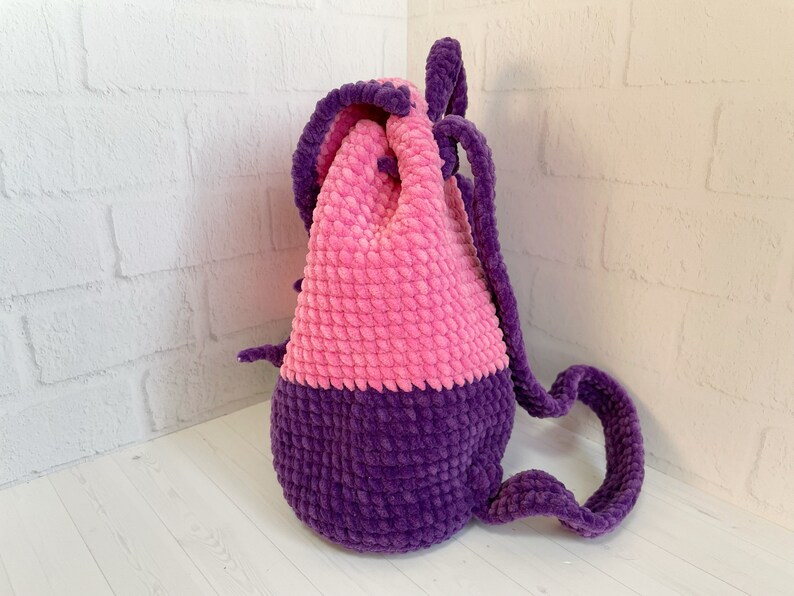 Pu&ograve; includere: Uno zaino con coulisse in crochet rosa e viola con una texture soffice.