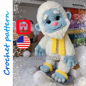 A plush crochet yeti with fluffy white fur, a light blue face, large sparkling eyes, and a pink nose wears a yellow scarf and gray slippers. The cover includes "Crochet pattern," a PDF download icon, and an American flag.