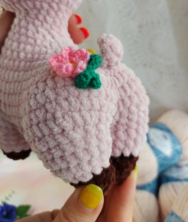 May include: A pink crocheted stuffed animal with brown feet and a flower on its back. The flower is pink with green leaves.