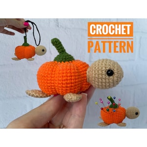 May include: A crochet turtle with an orange pumpkin-shaped shell, a green stem, and a tan head with black eyes. The image includes text that reads CROCHET PATTERN, a small hanging version with a black cord, and a version holding colorful pins.
