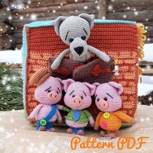 May include: Three crocheted pig figurines with different coloured outfits stand in front of a crocheted house with a wolf peeking out of the window. The house is made of orange, brown, and yellow yarn. The pigs are pink and have black eyes and noses. The wolf is grey and has black eyes and a black nose. The text "Pattern PDF" is written in orange letters at the bottom of the image.