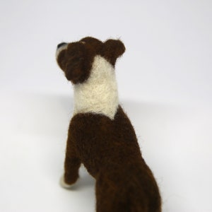 May include: A handmade felt dog figurine in a standing pose. The dog has a brown body with a white chest and neck. The dog's head is also brown with a white patch. The figurine is set against a white background.