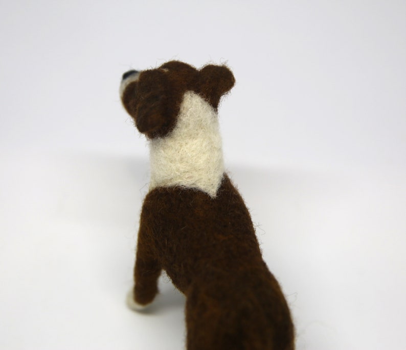 May include: A handmade felt dog figurine in a standing pose. The dog has a brown body with a white chest and neck. The dog's head is also brown with a white patch. The figurine is set against a white background.