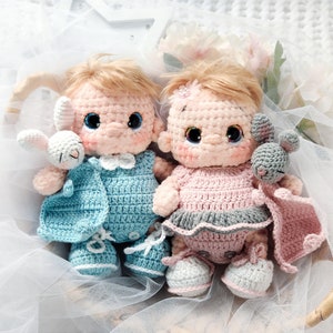 Pu&ograve; includere: Due bambole all'uncinetto, una in blu e una in rosa, tengono in braccio dei compagni di peluche. Le bambole indossano abiti all'uncinetto e hanno tratti del viso ricamati.