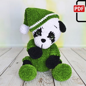 May include: A green and white crocheted panda bear wearing a green elf hat. The panda bear is sitting on a white wooden surface.