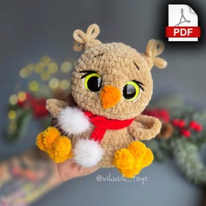 Könnte beinhalten: Ein gehäkeltes Eulen-Plüschtier mit großen Augen, einem roten Schal und gelben und weißen Akzenten. Die Eule hält einen weißen Pompon in ihren Pfoten.  @vilkusiik_toys