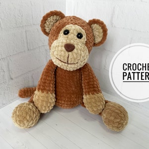 Puede incluir: Un mono de peluche de color marrón tejido a crochet con una cara sonriente y ojos negros. El juguete está sentado sobre una superficie blanca con el texto "CROCHET PATTERN" en un círculo.