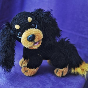 K&ouml;nnte beinhalten: Ein schwarzes und braunes geh&auml;keltes Pl&uuml;schtierhund mit langen, flauschigen Ohren und einem Schwanz. Der Hund hat einen freundlichen Ausdruck mit schwarzen Augen und einer rosa Zunge.