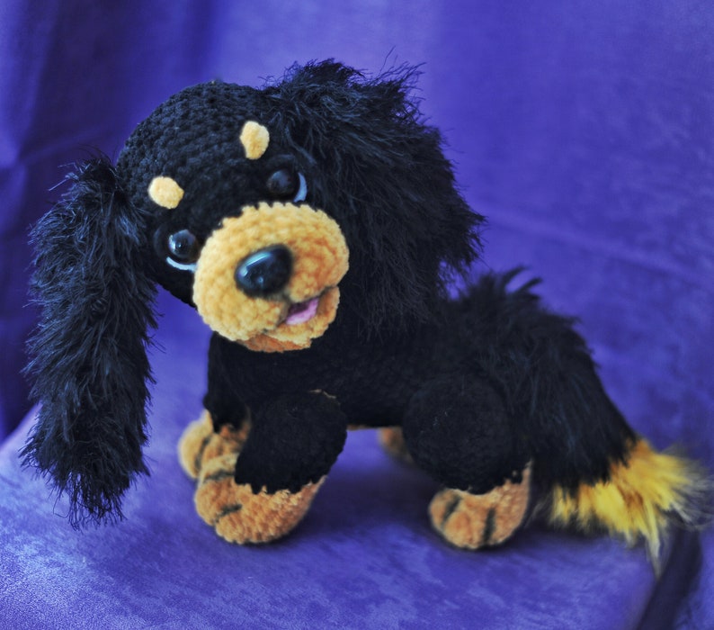 K&ouml;nnte beinhalten: Ein schwarzes und braunes geh&auml;keltes Pl&uuml;schtierhund mit langen, flauschigen Ohren und einem Schwanz. Der Hund hat einen freundlichen Ausdruck mit schwarzen Augen und einer rosa Zunge.
