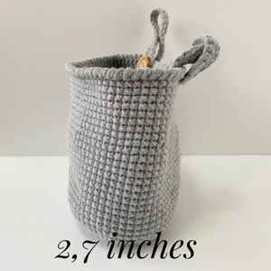 May include: A gray crocheted hanging basket with a wooden button detail. The basket is 2.7 inches tall.