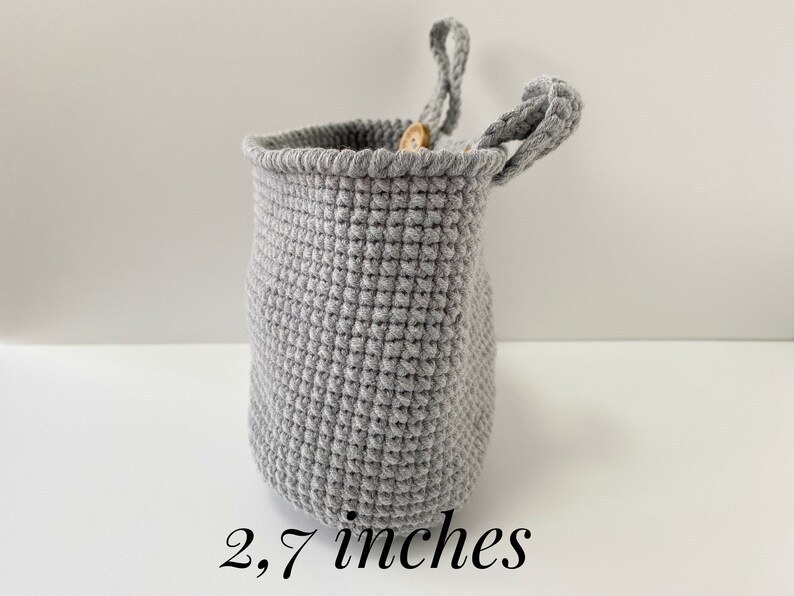 May include: A gray crocheted hanging basket with a wooden button detail. The basket is 2.7 inches tall.
