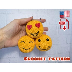 Op de afbeelding: Drie gele gehaakte emoji-sleutelhangers met verschillende gezichtsuitdrukkingen. Eén heeft hartogen, een ander een lachend gezicht en de derde een blij gezicht. De tekst "CROCHET PATTERN" staat onderaan de afbeelding.