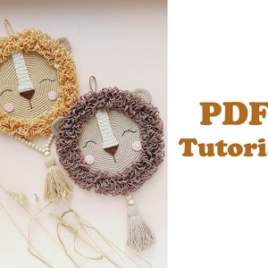 May include: Two crocheted lion wall hangings with brown and beige yarn. The lions have smiling faces with closed eyes and a brown nose. Each lion has a tassel hanging from the bottom. The text "PDF Tutorial" is in the background.