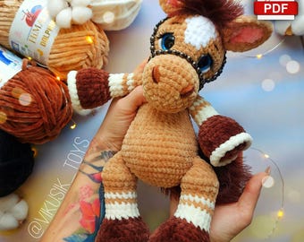 May include: A handmade plush horse toy in shades of brown, white, and dark brown. The horse has a white spot on its forehead, blue eyes, and a dark brown mane. The toy is held in someone's hands. The text "@VIKUSIK_TOYS" is visible.
