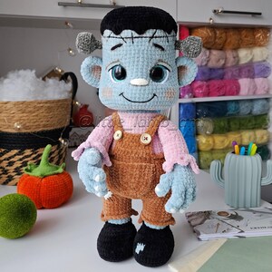 Handmade plush Frankenstein amigurumi with embroidered details and buttoned suspenders. Crochet pattern download for creating an adorable Halloween decoration or gift.
