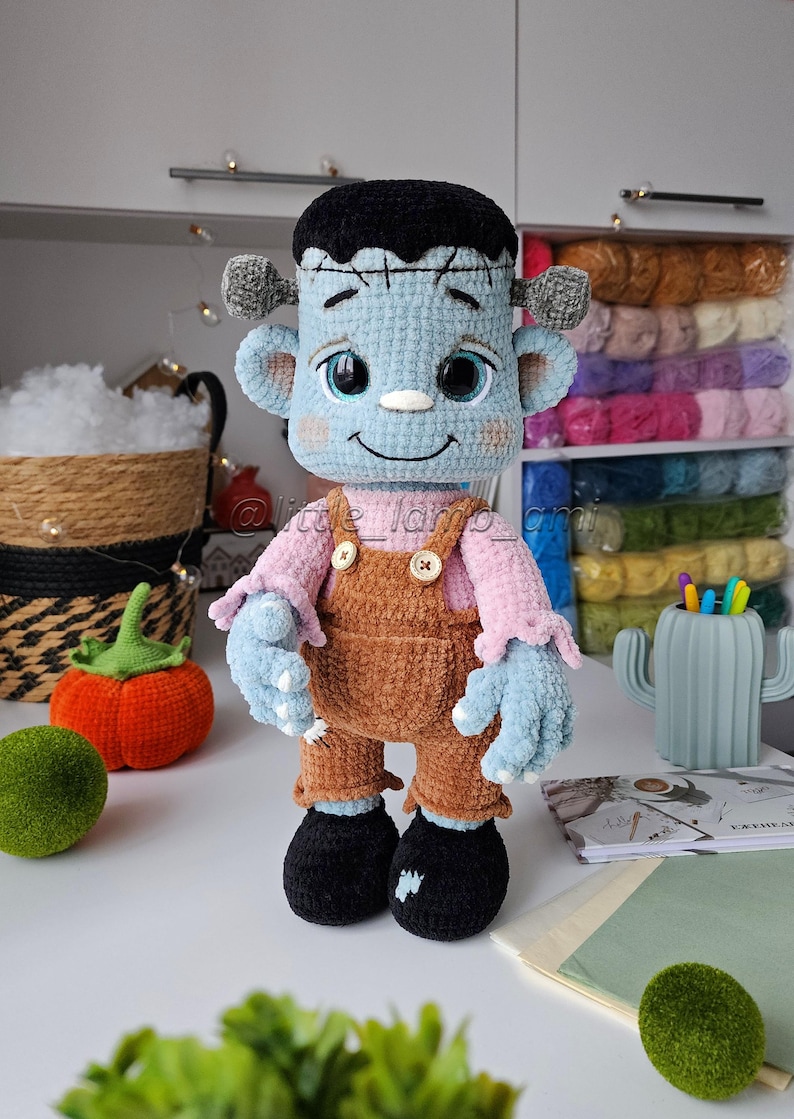 Handmade plush Frankenstein amigurumi with embroidered details and buttoned suspenders. Crochet pattern download for creating an adorable Halloween decoration or gift.