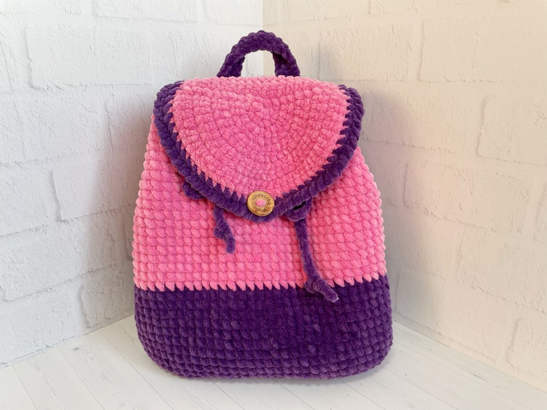 Pu&ograve; includere: Uno zaino in crochet rosa e viola con chiusura a bottone e coulisse.