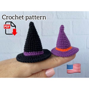 Può includere: Due cappelli da strega all'uncinetto in miniatura, uno nero con una fascia viola e l'altro viola con una fascia arancione. I cappelli sono esposti su un dito. L'immagine include il testo "Crochet pattern" e un'icona PDF.