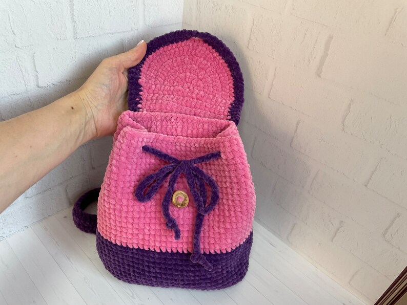 Pu&ograve; includere: Uno zaino in crochet rosa e viola con chiusura a coulisse e un bottone in legno. Lo zaino &egrave; realizzato con un filato morbido e testurizzato.