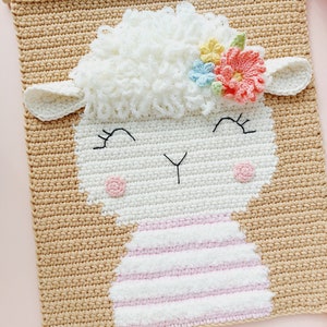 May include: A crocheted wall hanging featuring a white sheep with a pink and white striped dress and a flower crown with pink, blue, and yellow flowers. The sheep has a smiling face with black eyes and a black nose.