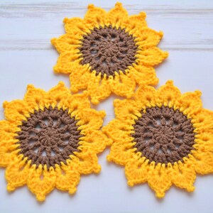 May include: Three crocheted sunflower coasters in yellow and brown. The coasters are made with a detailed pattern and have a raised center.