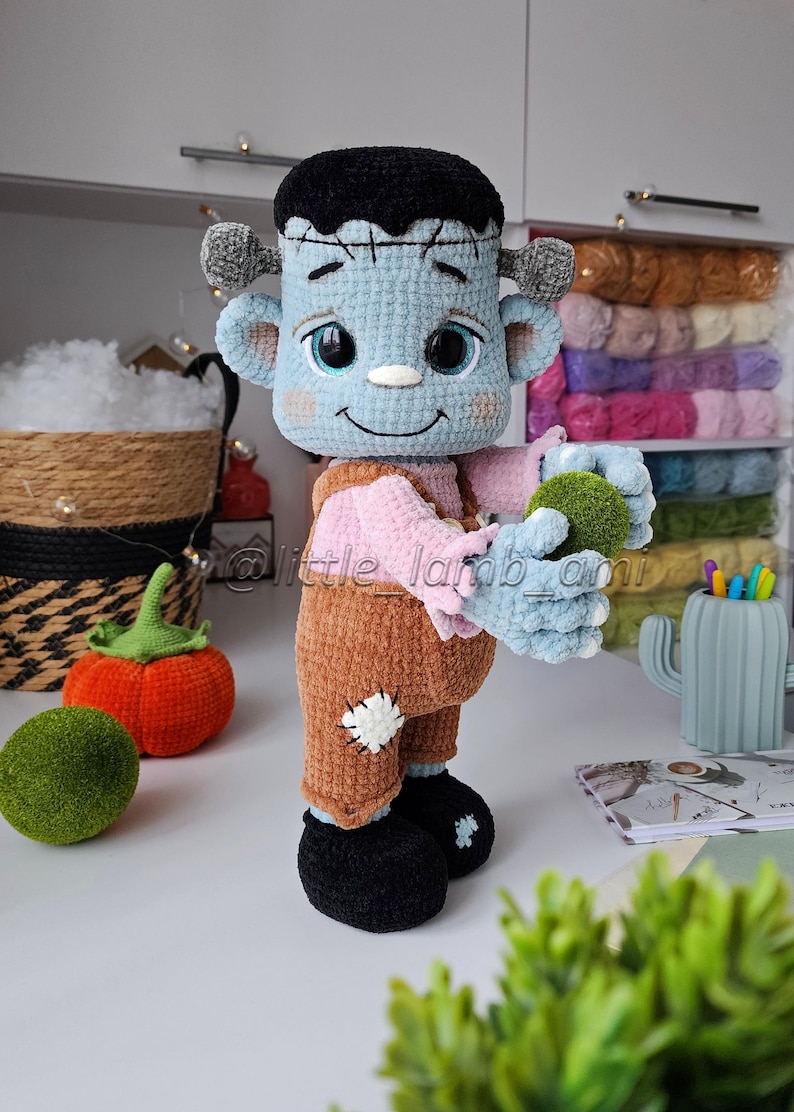 Crocheted Frankenstein plush holding a green ball, surrounded by cozy yarn and autumn decor. Fun Halloween crochet project with clear step-by-step instructions.