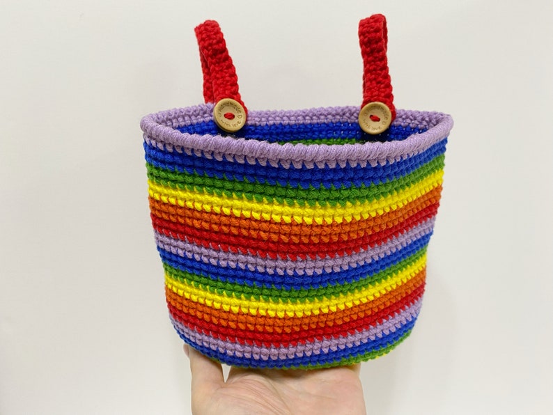 May include: A rainbow striped crocheted basket with red handles and wooden button accents.