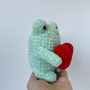 May include: A green crocheted frog holding two red crocheted hearts.