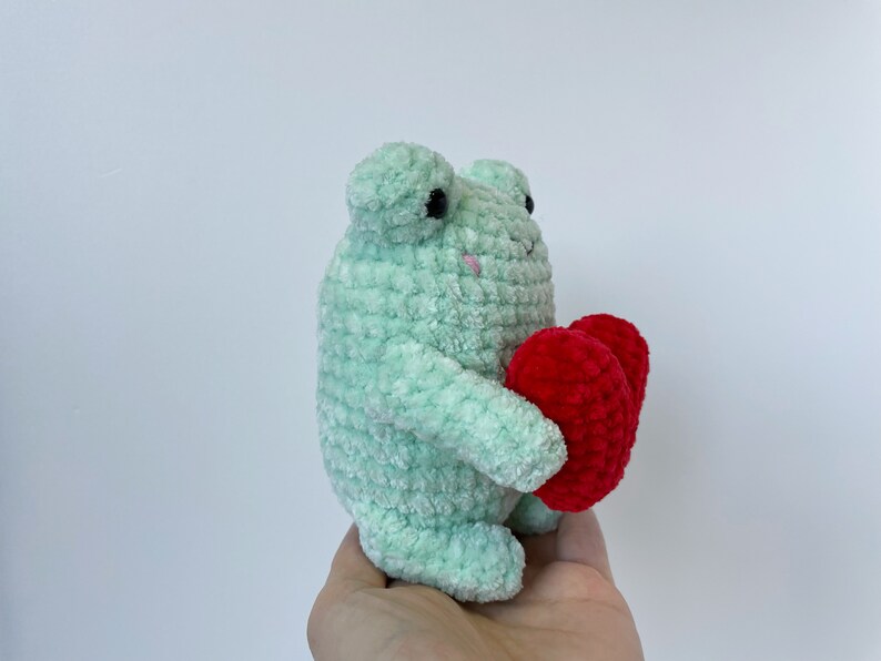 May include: A green crocheted frog holding two red crocheted hearts.