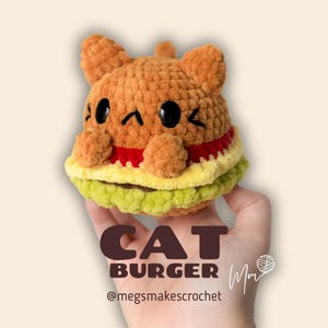 Könnte beinhalten: Ein gehäkelter Burger in Katzenform mit einem braunen Brötchen, rotem Ketchup, gelbem Käse und grünem Salat. Der Text "CAT BURGER" und "Mm" steht unter dem Bild. Der Text "@megsmakescrochet" steht unter dem Text.