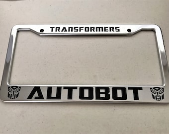 May include: A silver metal license plate frame with black text that reads "TRANSFORMERS AUTOBOT" and features the Autobot symbol on each side.