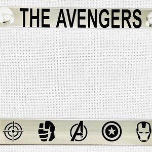 May include: A silver metal license plate frame with the text "THE AVENGERS" in black lettering. The frame features seven black icons of the Avengers characters: Thor's hammer, Hawkeye's target, Hulk's fist, Captain America's shield, Iron Man's mask, Black Widow's hourglass, and the Avengers logo.