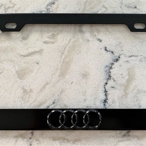 May include: Black metal license plate frame with the Audi logo in the center.