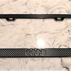 Peut inclure: Cadre de plaque d'immatriculation en fibre de carbone noire avec un logo Audi argenté.