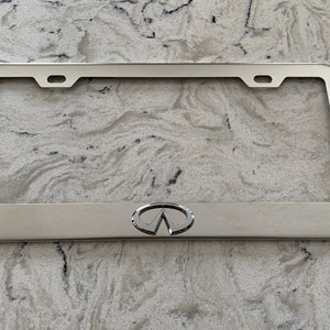 May include: Silver metal license plate frame with the Infiniti logo in the center.