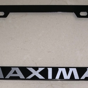 Peut inclure: Cadre de plaque d'immatriculation en métal noir avec une inscription "MAXIMA" argentée.