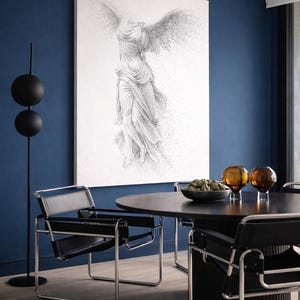 Puede incluir: Una obra de arte enmarcada que representa una figura alada en escala de grises. La habitación presenta una pared azul oscuro, una mesa de comedor negra y sillas de cuero negro con marcos cromados. También se ven esferas decorativas de vidrio y una lámpara de pie negra.