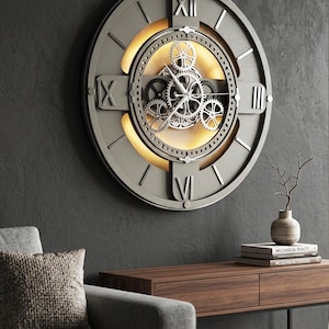 May include: A large circular wall clock with a dark gray frame and Roman numerals. The center features an exposed mechanical gear system illuminated by a warm internal light. The clock face has a layered design with metallic silver accents and visible rotating gears behind the hands.