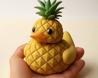May include: A whimsical, handcrafted figurine of a duck with a pineapple design. The duck has a yellow body with a textured pattern, an orange beak, and black eyes. The top of the duck is a green pineapple crown. The figurine is held in a hand.