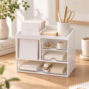 May include: A white desk organiser with multiple compartments and three clear drawers. The unit holds stationery including a notepad labelled A BRIGHTER DAY, a THINGS TO DO list, a ribbed pen cup with gold pens and scissors, and various paper supplies.
