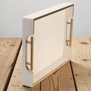 May include: A rectangular serving tray with a cream-colored interior and exterior, accented with gold trim and handles. The tray has a textured, ribbed side and is set on a wooden surface.
