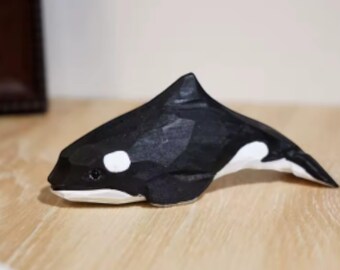 May include: Hand-carved wooden orca figurine. The orca is painted black and white, with white patches near the eyes and belly. The figurine has a pointed dorsal fin and a streamlined body, perfect for home decor or a gift.