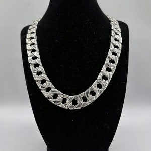 May include: A silver chain necklace with a large, intricate link design. The chain is displayed on a black velvet stand.