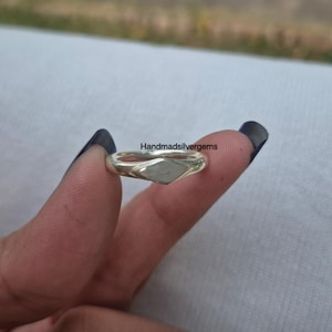 May include: A silver ring with a diamond-shaped face. The ring is held between two fingers. The text "Handmadsilvergems" is visible in the image. The ring is a piece of jewellery.