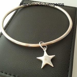May include: A silver-colored bangle bracelet with a star charm. The star charm is suspended from a small loop attached to the bracelet. The text "Handmadsilvergems" is visible on the background.