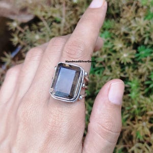 Könnte beinhalten: Ein Silberring mit einem großen, rechteckigen Rauchquarz-Edelstein. Der Ring hat ein detailliertes Band mit dekorativen Elementen und dem Text "HandmadSilverGems". Der Edelstein hat eine transluzente braune Farbe.