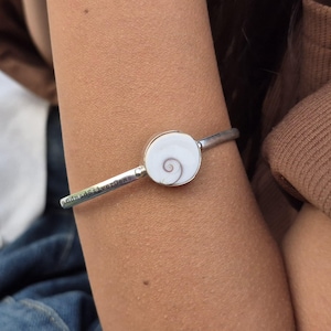 Może przedstawiać: Srebrna bransoletka z białym, spiralnym wzorem. Bransoletka ma wygrawerowany napis "andmadSilverGems" na opasce. Bransoletka jest noszona na ramieniu.