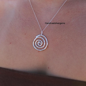 Puede incluir: Un collar con colgante de plata con diseño de espiral. El colgante cuelga de una fina cadena. El collar se muestra sobre un fondo neutro. El texto "Handmadsilvergems" es visible en la imagen.